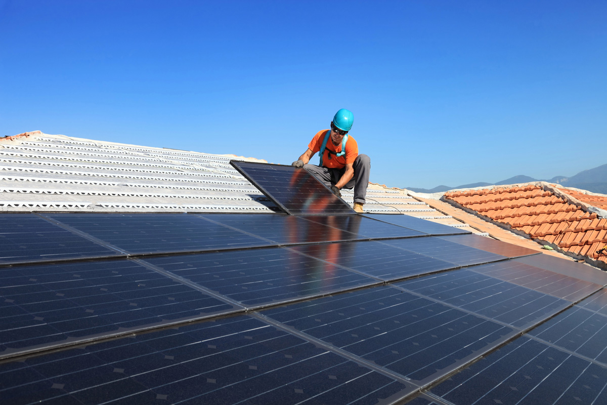 Worker installing photovoltaic solar panels on roof